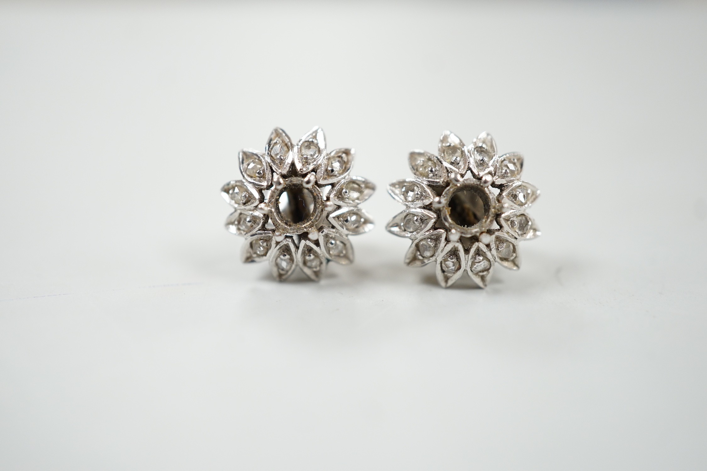 A cased pair of white metal and diamond cluster set flower head ear studs, both lacking centre stone, diameter 13mm, gross weight 4.4 grams.